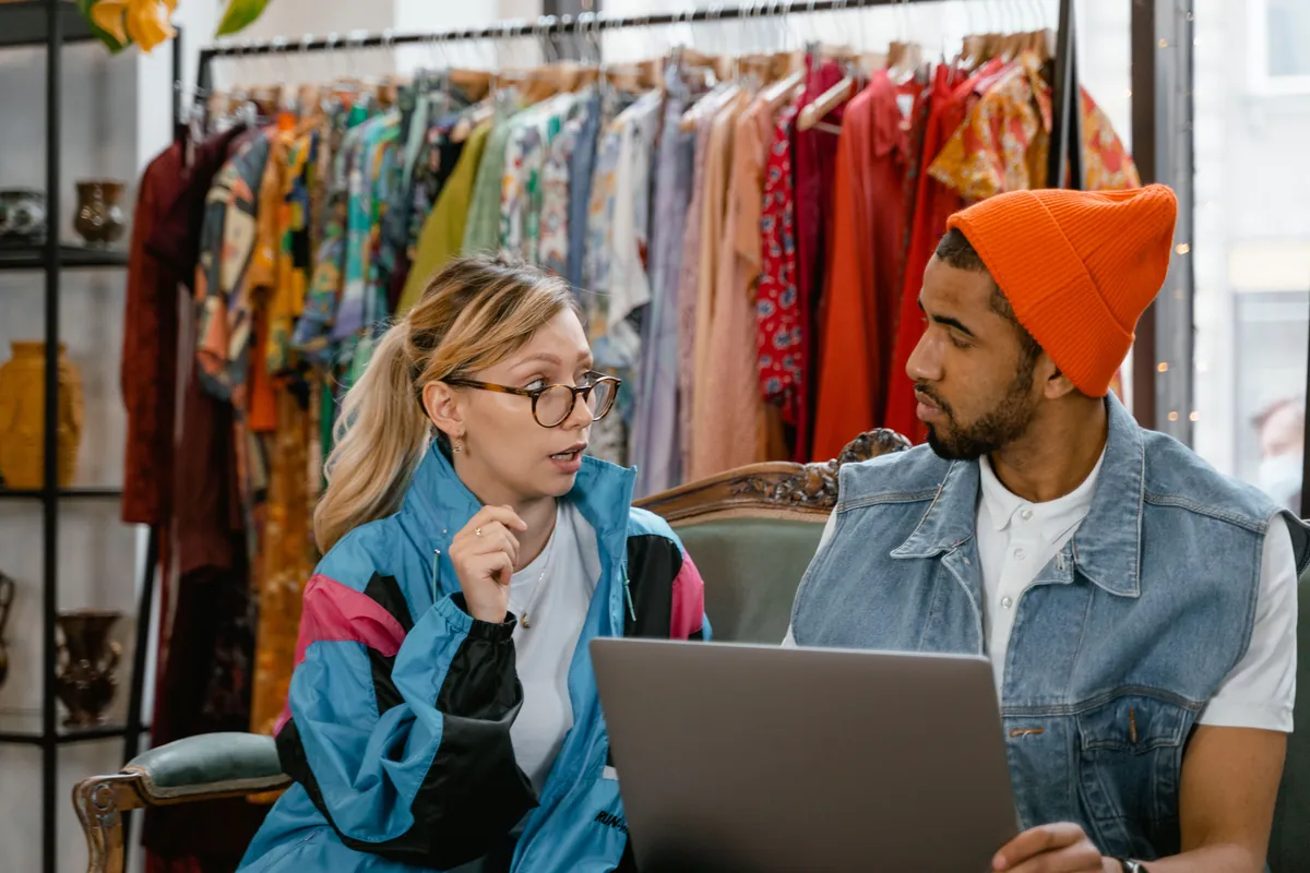 Dos personas manejando una tienda de ropa desde una laptop, entre los percheros