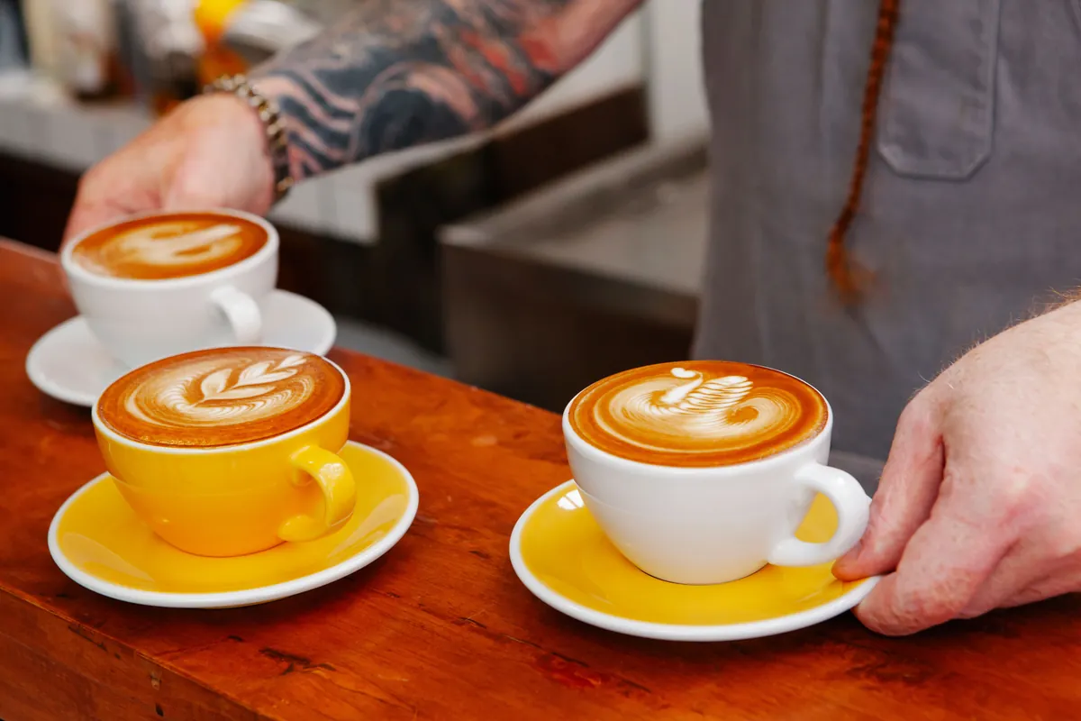 Un barista pone tres lattes con arte en la espuma sobre la barra de madera de una cafetería