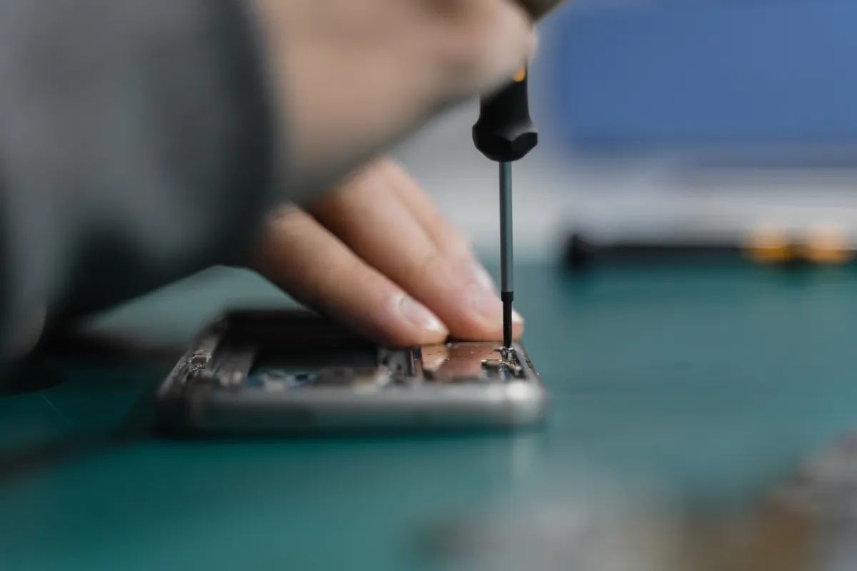 Los dedos de un técnico aprietan un tornillo diminuto de un celular abierto