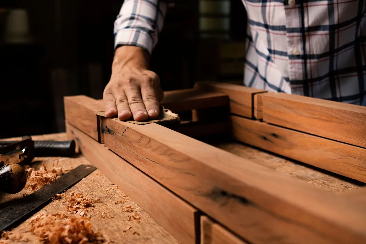 La mano de un carpintero lija un marco de madera en un banco de trabajo lleno de virutas