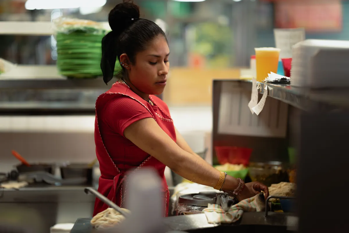 Una cocinera en la plancha de la cocina de un comedor con mucho trabajo, con las comandas a la par